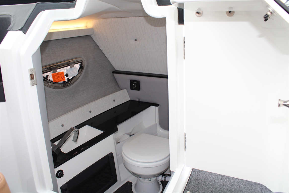 Interior view of a boat's bathroom featuring a toilet, sink, and a window, with modern gray and white decor.